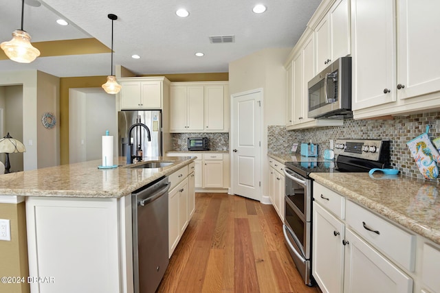 kitchen with hanging light fixtures, sink, an island with sink, light wood-type flooring, and appliances with stainless steel finishes