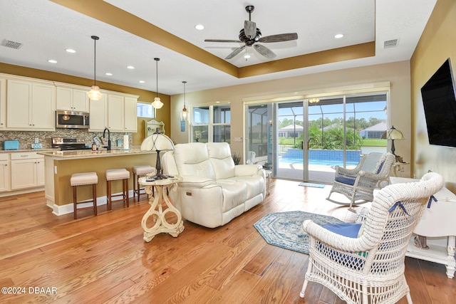 living room with light hardwood / wood-style floors, ceiling fan, a raised ceiling, and sink