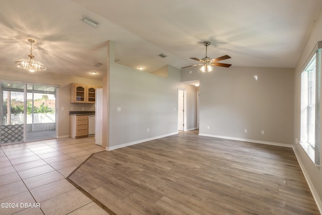 unfurnished living room featuring plenty of natural light, ceiling fan with notable chandelier, light tile patterned flooring, and lofted ceiling