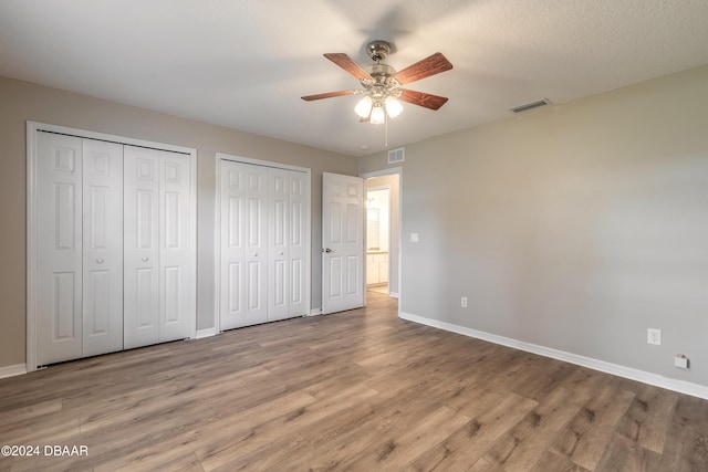 unfurnished bedroom featuring two closets, light hardwood / wood-style floors, and ceiling fan