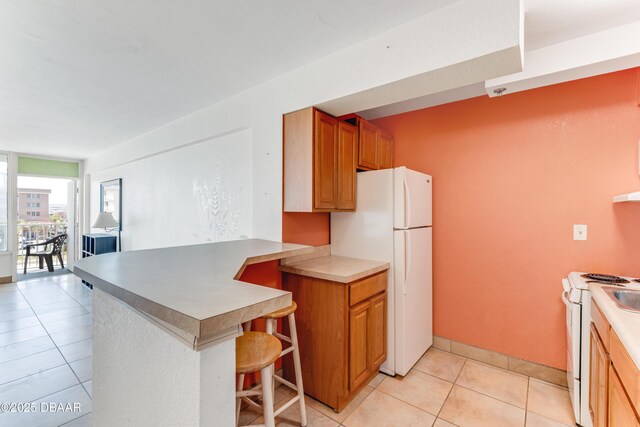 kitchen featuring sink, light tile patterned floors, white appliances, and kitchen peninsula