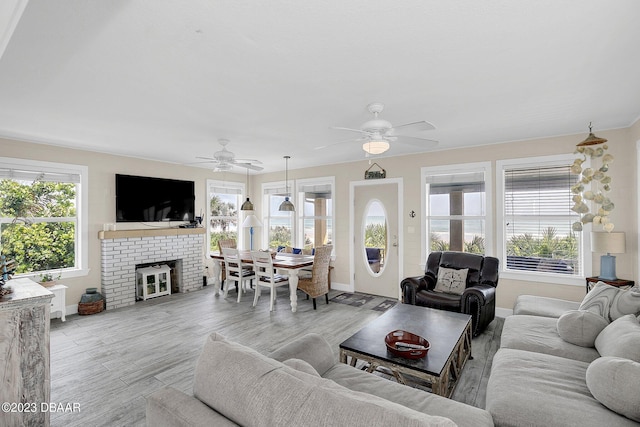 living room featuring a brick fireplace, light wood-type flooring, a wealth of natural light, and ceiling fan