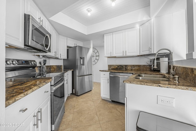 kitchen featuring stainless steel appliances, a tray ceiling, sink, light tile patterned floors, and white cabinetry