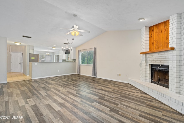 unfurnished living room featuring hardwood / wood-style floors, a textured ceiling, lofted ceiling, a fireplace, and ceiling fan with notable chandelier