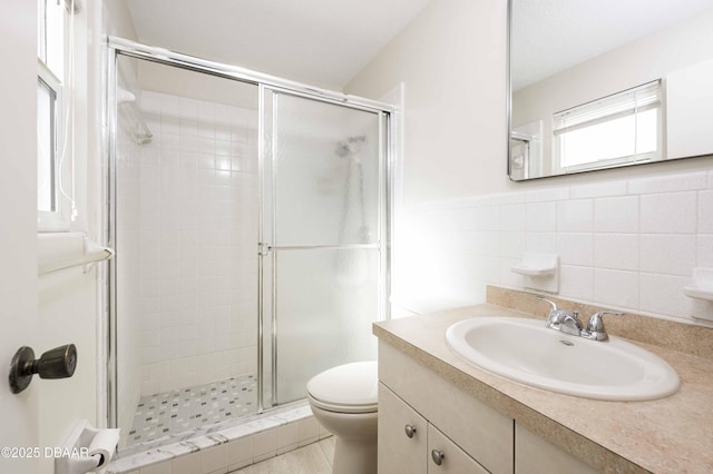 bathroom featuring vanity, toilet, a shower with door, and tile walls