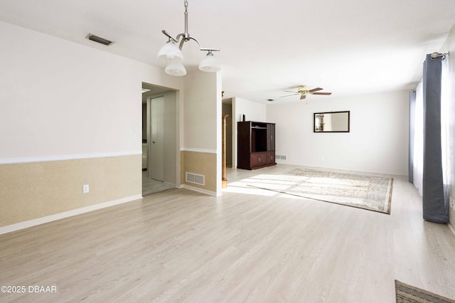 unfurnished living room featuring ceiling fan with notable chandelier and light hardwood / wood-style flooring