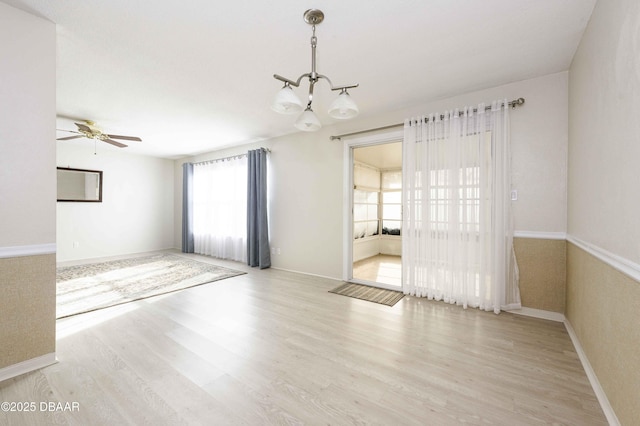 empty room featuring ceiling fan with notable chandelier and light hardwood / wood-style flooring