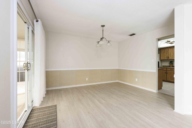 empty room with a notable chandelier and light hardwood / wood-style flooring