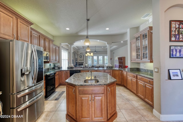 kitchen with dark stone counters, black appliances, a center island with sink, ornate columns, and kitchen peninsula