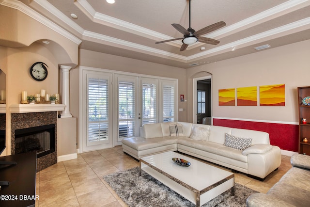 tiled living room featuring a tile fireplace, a raised ceiling, ceiling fan, and ornamental molding