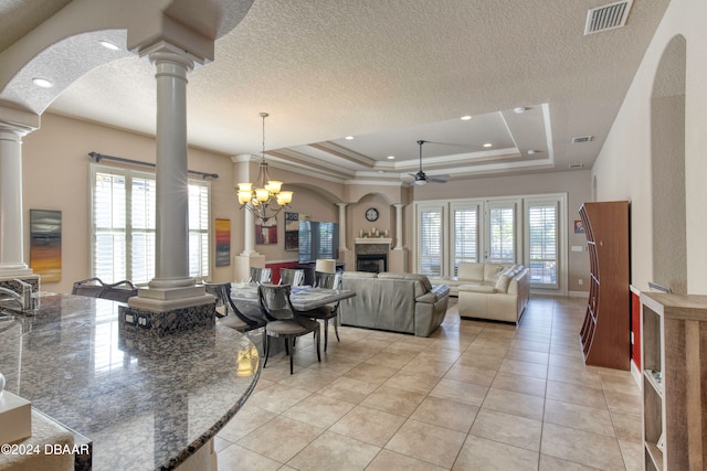 living room featuring a raised ceiling, light tile patterned floors, a healthy amount of sunlight, and ceiling fan with notable chandelier