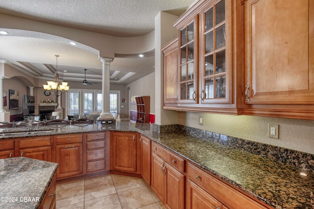 kitchen with decorative columns, sink, dark stone counters, and a textured ceiling