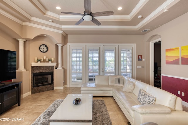 tiled living room featuring a tray ceiling, ornate columns, crown molding, and ceiling fan