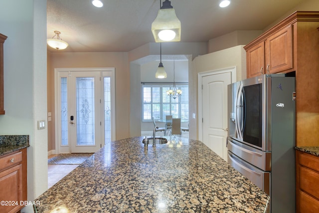 kitchen with decorative light fixtures, stainless steel fridge, dark stone counters, and a chandelier