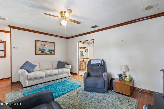 living room with wood finished floors, visible vents, ornamental molding, and ceiling fan