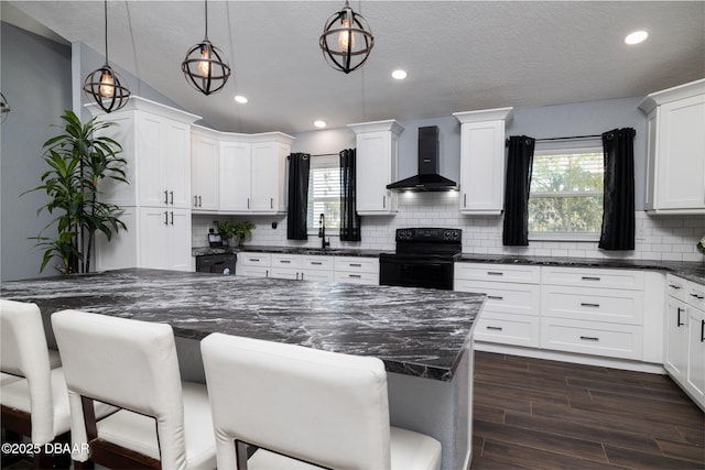 kitchen featuring tasteful backsplash, black range with electric stovetop, wood finish floors, wall chimney range hood, and a kitchen bar