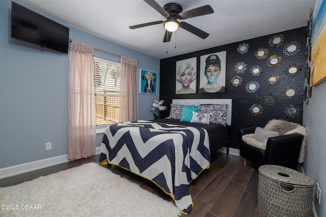 bedroom featuring a textured ceiling, an accent wall, baseboards, ceiling fan, and wood tiled floor