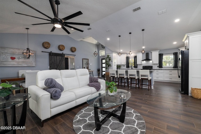 living room featuring visible vents, a barn door, ceiling fan, dark wood-style flooring, and vaulted ceiling