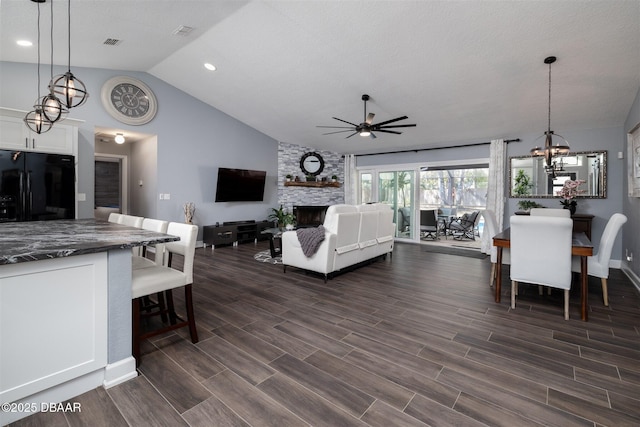 living room with a stone fireplace, ceiling fan with notable chandelier, visible vents, and wood tiled floor