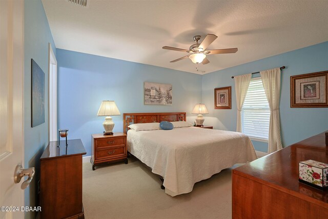 bedroom featuring ceiling fan, light colored carpet, and a textured ceiling