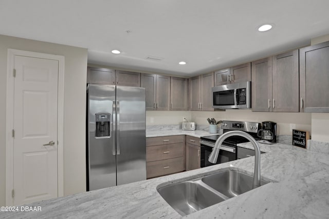 kitchen with appliances with stainless steel finishes, sink, and light stone countertops