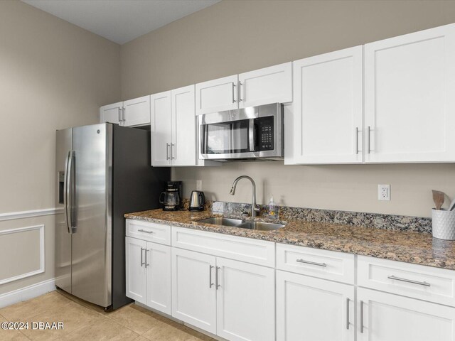 kitchen with stainless steel appliances, sink, light tile patterned floors, white cabinetry, and dark stone countertops