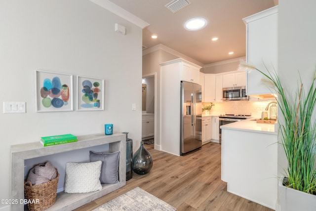 kitchen with appliances with stainless steel finishes, backsplash, ornamental molding, white cabinets, and light hardwood / wood-style floors