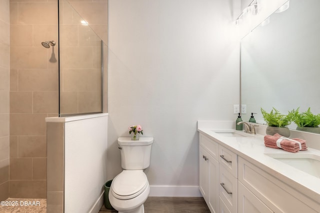 bathroom with vanity, toilet, a tile shower, and wood-type flooring