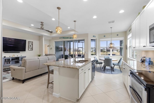 kitchen with light stone counters, a kitchen island with sink, sink, and white cabinets