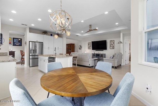 tiled dining area featuring ceiling fan with notable chandelier, a tray ceiling, and sink