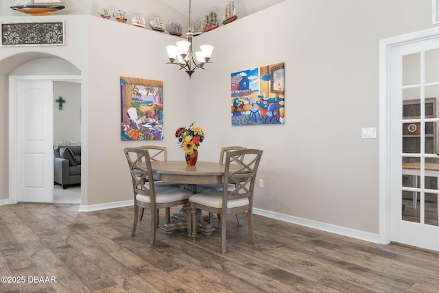 dining area featuring a chandelier, arched walkways, baseboards, and wood finished floors