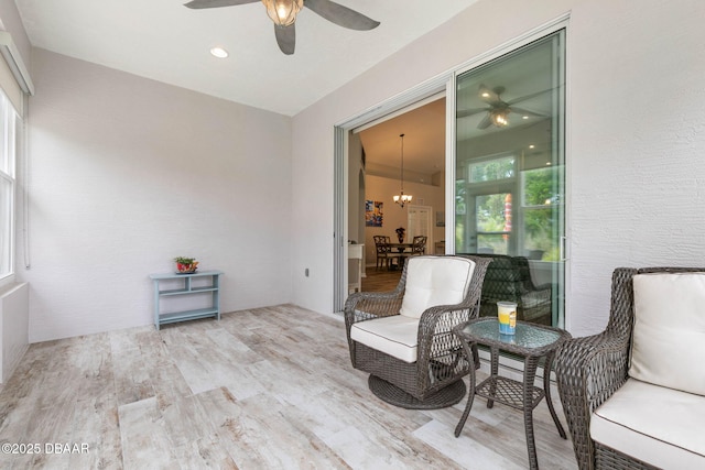 living area featuring ceiling fan with notable chandelier and wood finished floors