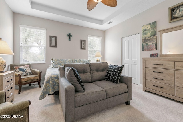 bedroom with a tray ceiling, a closet, light carpet, and ceiling fan