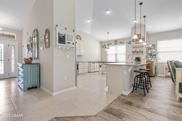 kitchen with baseboards, lofted ceiling, light stone counters, a breakfast bar, and hanging light fixtures