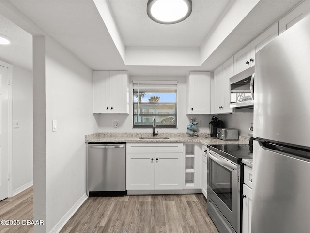 kitchen featuring appliances with stainless steel finishes, sink, white cabinets, a tray ceiling, and light wood-type flooring