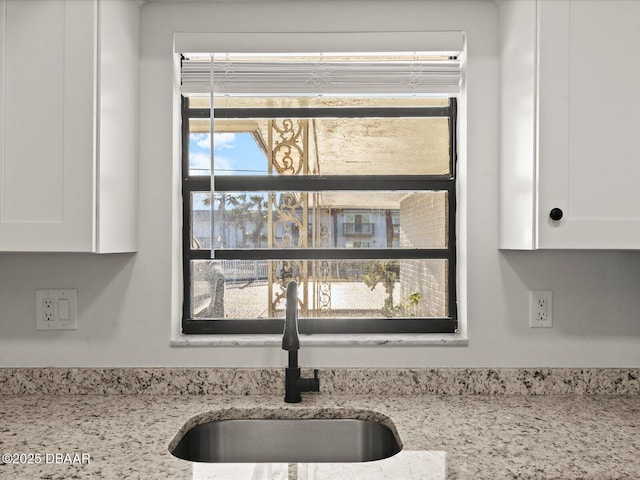 interior details featuring white cabinetry, sink, and light stone countertops