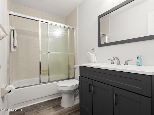 full bathroom featuring vanity, hardwood / wood-style floors, enclosed tub / shower combo, and toilet