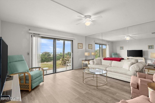 living room with a textured ceiling, ceiling fan, and light wood-type flooring