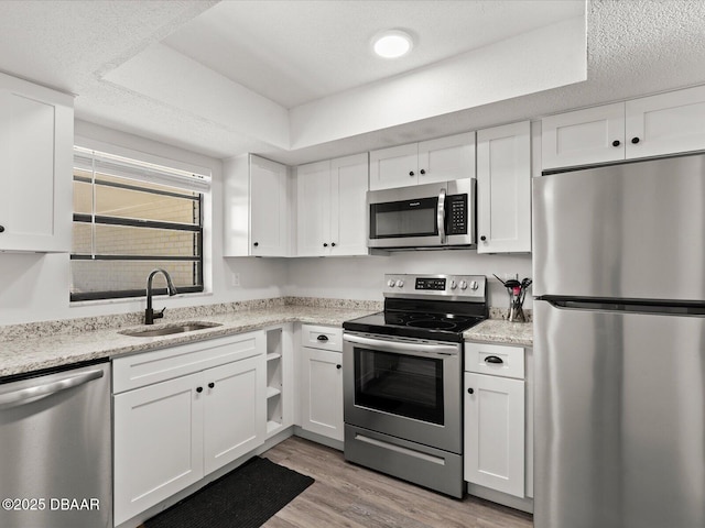 kitchen with sink, white cabinetry, stainless steel appliances, a tray ceiling, and light hardwood / wood-style floors