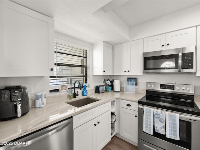 kitchen featuring appliances with stainless steel finishes, sink, white cabinets, light stone counters, and dark wood-type flooring