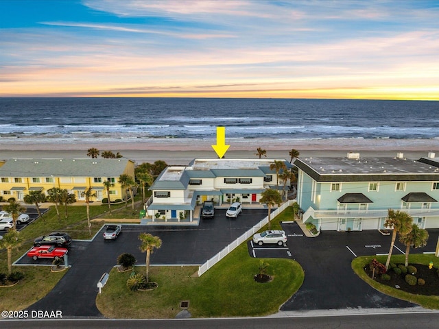 aerial view at dusk featuring a view of the beach and a water view