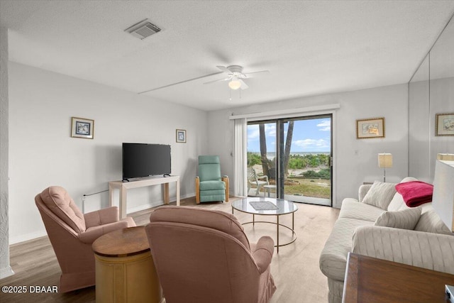 living room with ceiling fan, a textured ceiling, and light wood-type flooring