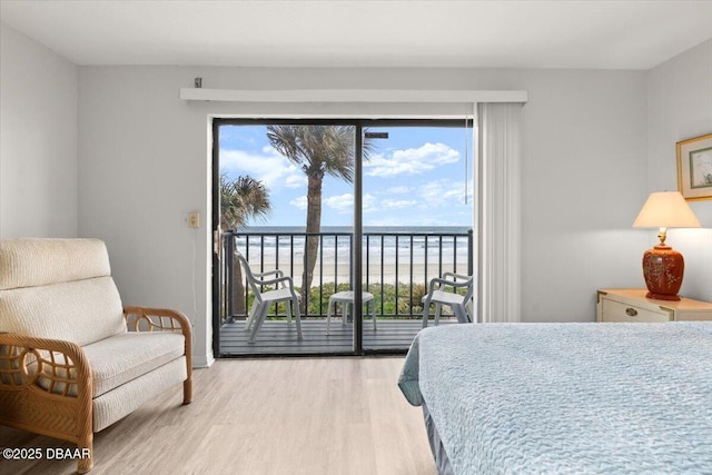 bedroom with a view of the beach, access to outside, light hardwood / wood-style flooring, and a water view