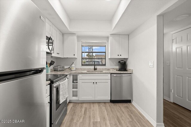 kitchen featuring a raised ceiling, white cabinetry, appliances with stainless steel finishes, and sink