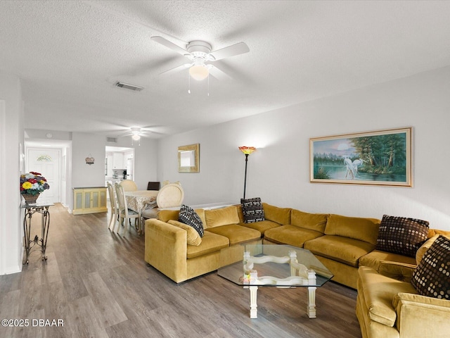 living room with ceiling fan, hardwood / wood-style flooring, and a textured ceiling