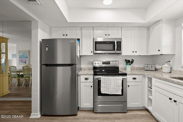 kitchen featuring white cabinetry, light hardwood / wood-style flooring, light stone countertops, and appliances with stainless steel finishes