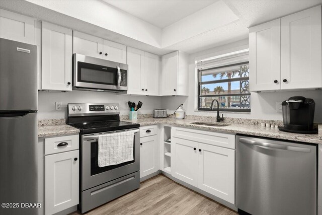 kitchen with stainless steel appliances, sink, light hardwood / wood-style flooring, and white cabinets