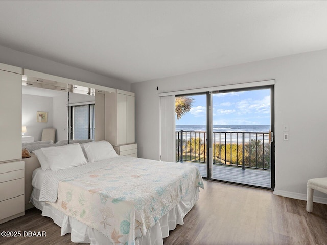 bedroom with a beach view, a water view, hardwood / wood-style floors, and access to exterior