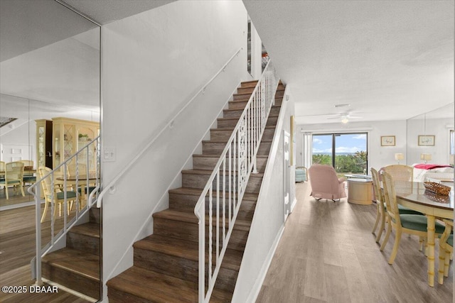 stairway with hardwood / wood-style flooring, a textured ceiling, and ceiling fan