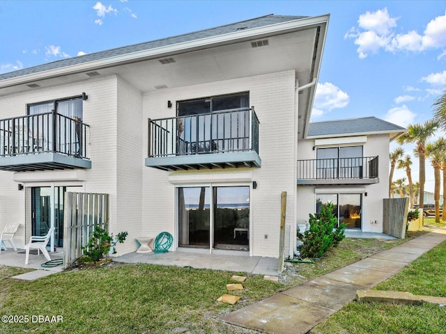 rear view of property featuring a patio, a balcony, and a lawn